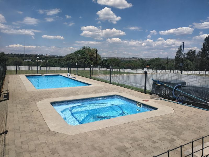 Communal outdoor area featuring a swimming pool and a smaller plunge pool set within a paved enclosure with secure perimeter fencing.