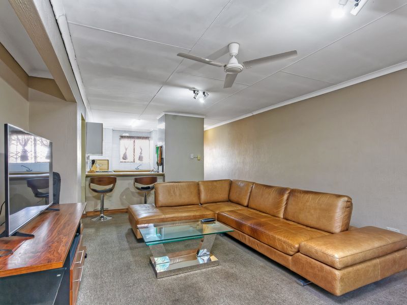Open plan living area featuring a breakfast bar, kitchen cabinetry, and a ceiling fan, with carpeted flooring throughout.