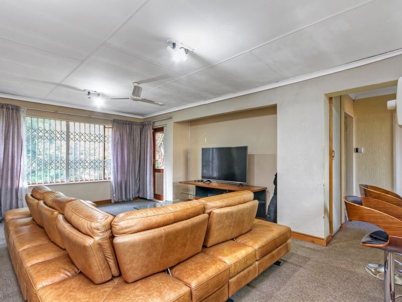 Spacious living room featuring carpeted flooring, a ceiling fan, and a recessed wall niche, with direct access to an outdoor area via a security gate.