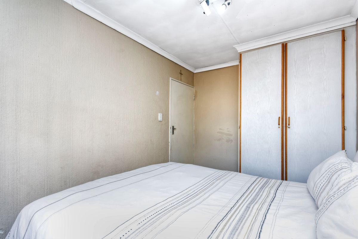 A bedroom featuring built-in cupboards and coving, showing signs of wear on the walls and ceiling that would benefit from cosmetic updates.