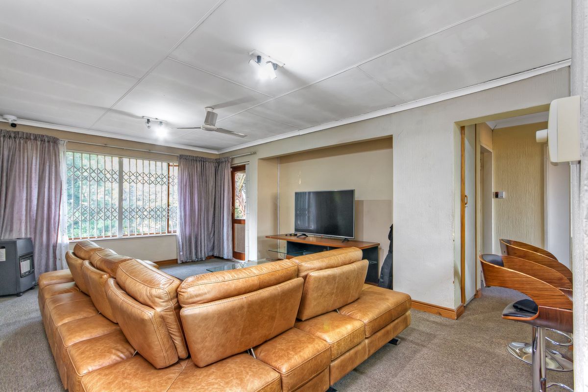 Spacious living room featuring carpeted flooring, a ceiling fan, and a recessed wall niche, with direct access to an outdoor area via a security gate.