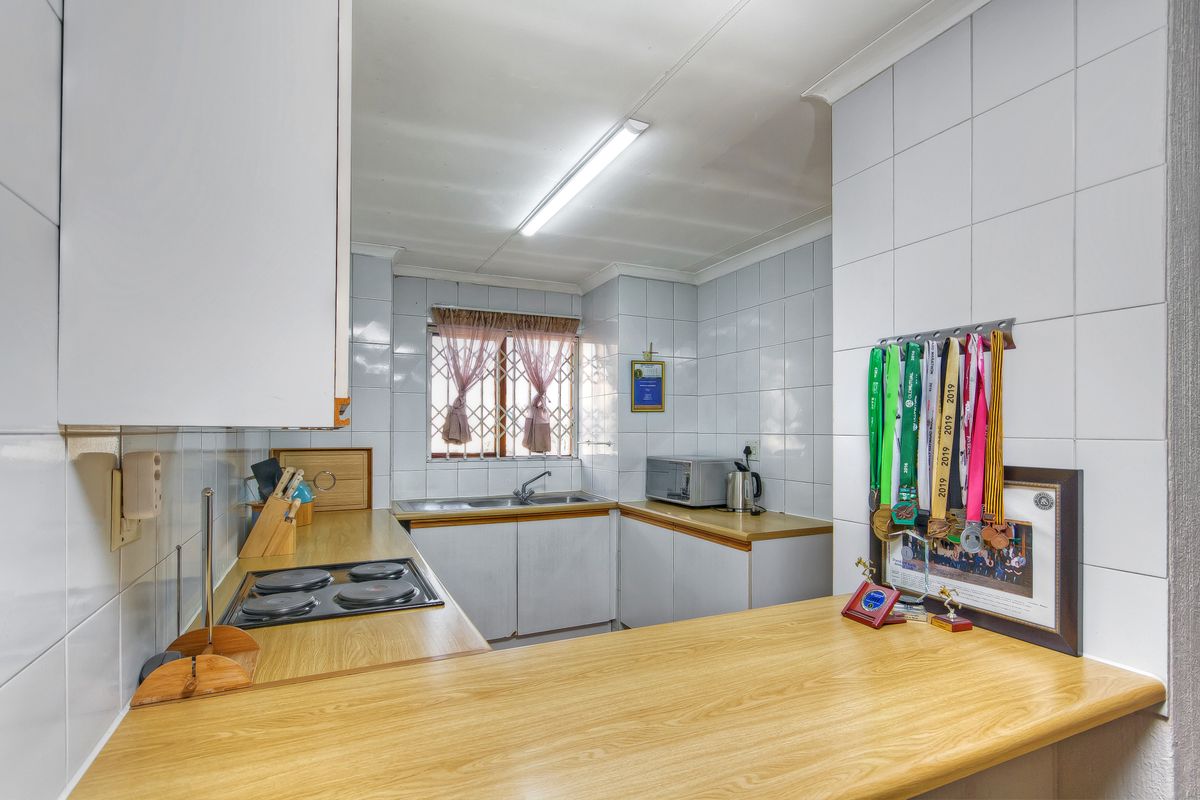 A functional kitchen featuring laminate countertops, an electric hob, double sink, and tiled splashbacks, offering a practical layout for daily meal preparation.