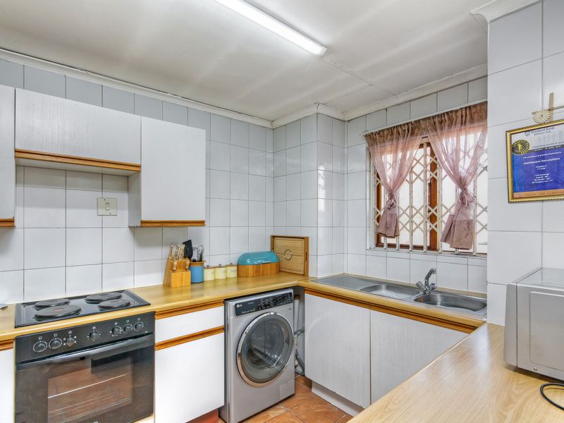 Functional kitchen featuring white cabinetry, laminate countertops, built-in electric oven and stove, double sink, and tiled splashbacks with a security-fitted window.