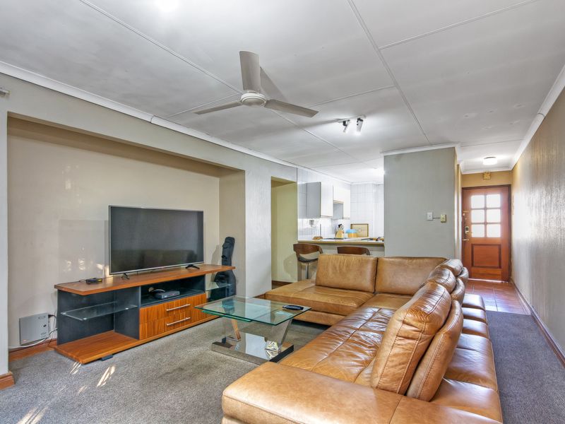 Open plan living area featuring a ceiling fan, carpeted flooring, and a connected kitchen space with built-in cabinetry and a tiled backsplash.