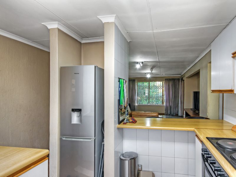 Open-plan kitchen and living area featuring laminate countertops, built-in cabinetry, and an electric hob, flowing into a naturally lit lounge space.