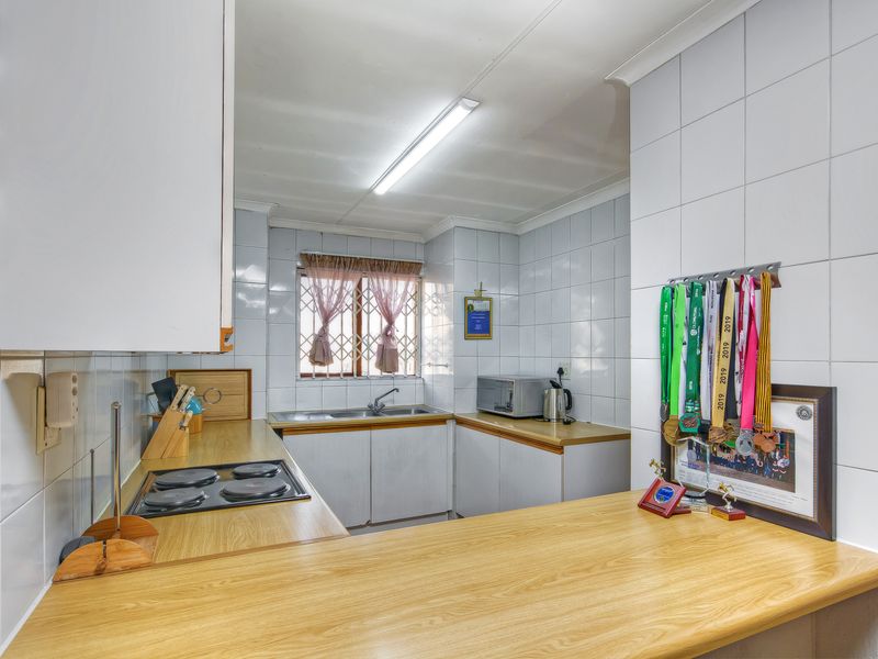 A functional kitchen featuring laminate countertops, an electric hob, double sink, and tiled splashbacks, offering a practical layout for daily meal preparation.
