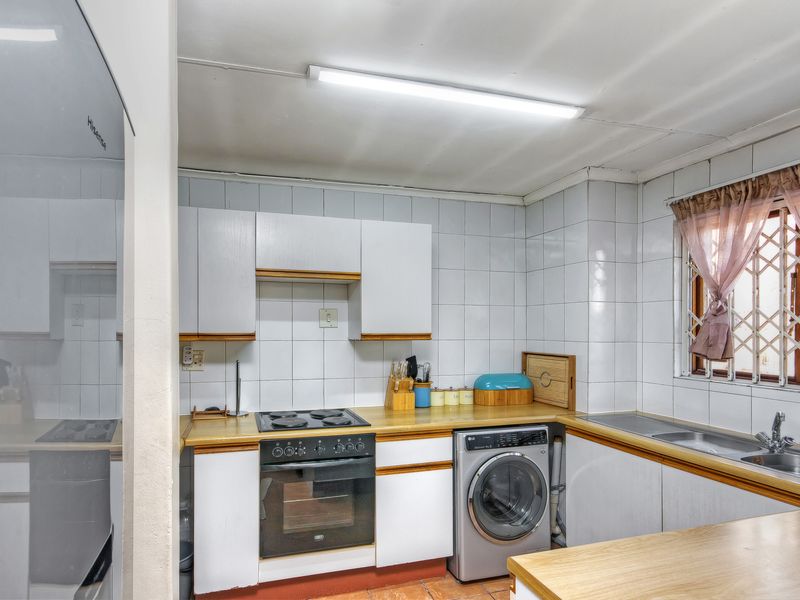 Functional kitchen featuring built-in cabinetry, electric hob, oven, and stainless steel sink with tiled backsplash and security window treatments.