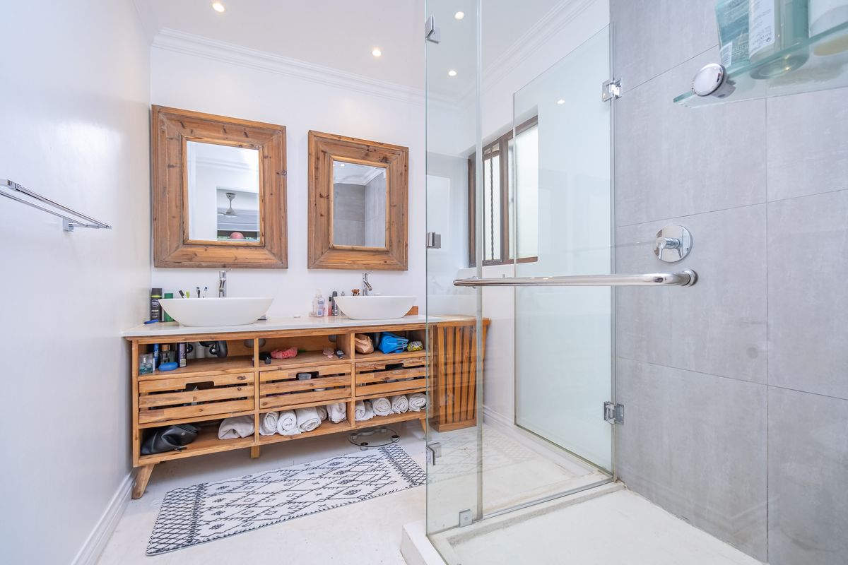 Modern bathroom featuring a double vanity with vessel sinks, wooden cabinetry, and a spacious walk-in shower with a frameless glass enclosure.
