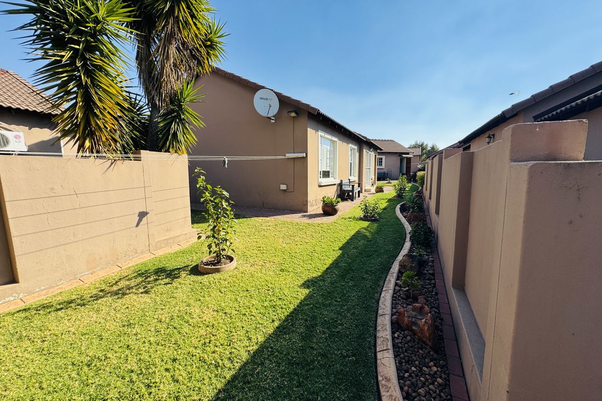 A well-maintained rear garden area featuring a manicured lawn, paved pathway, and high boundary walls for privacy.