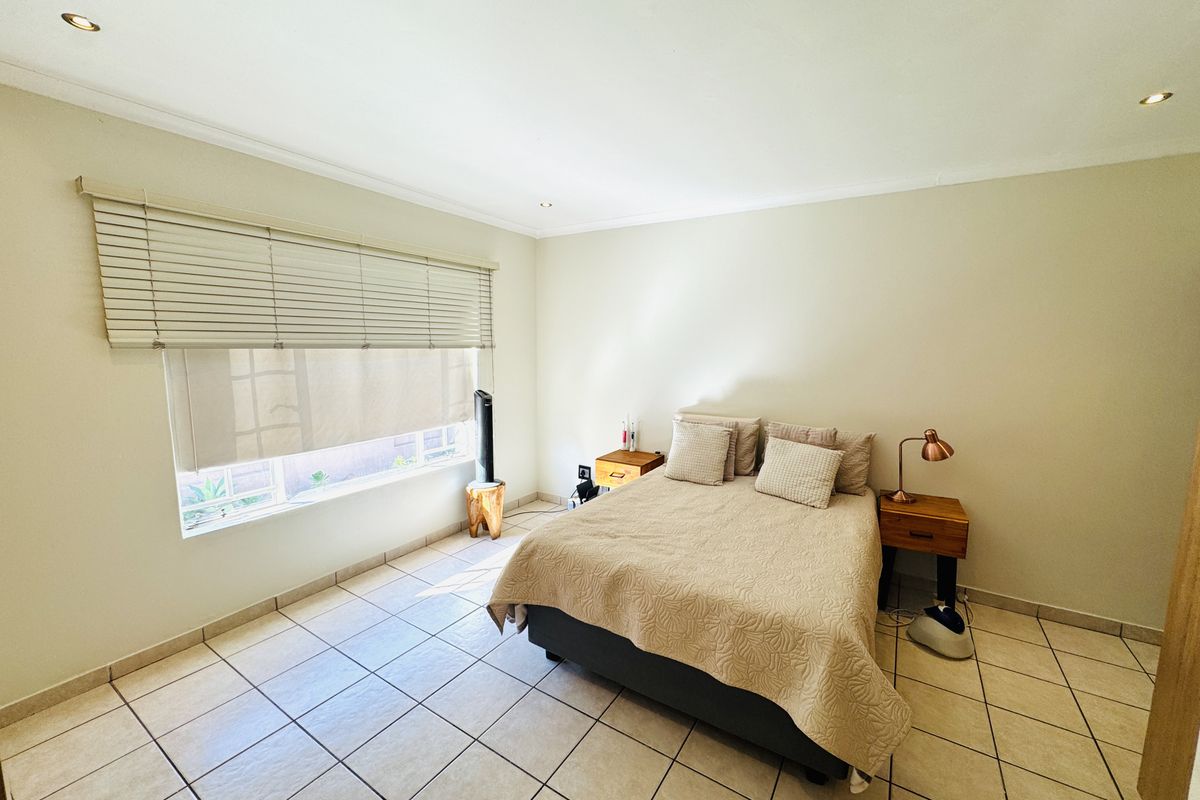 A well-lit bedroom featuring neutral walls, tiled flooring, and recessed downlighting, providing a clean and functional space.