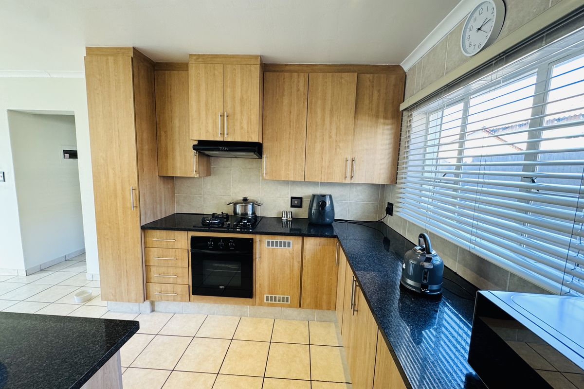 A functional kitchen featuring light wood cabinetry, dark granite countertops, built-in oven, gas hob, and tiled flooring with ample natural light.