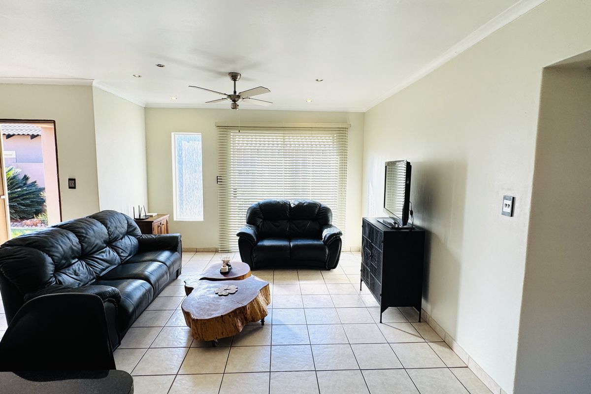 A bright and spacious living room featuring neutral tiled flooring, a ceiling fan, and large sliding glass doors that provide access to the outdoor area.