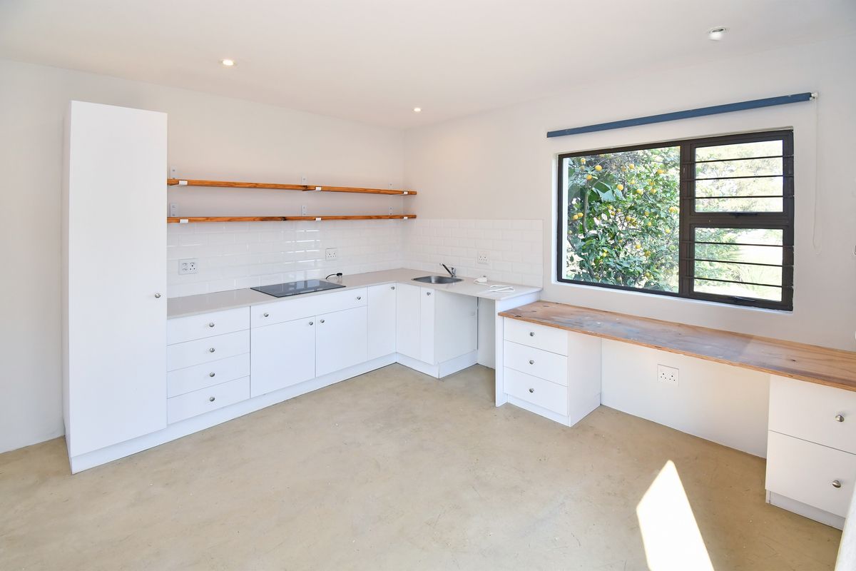 A clean, modern kitchen featuring white cabinetry, subway tile backsplash, wooden shelving, and a built-in hob, with ample natural light from the window.
