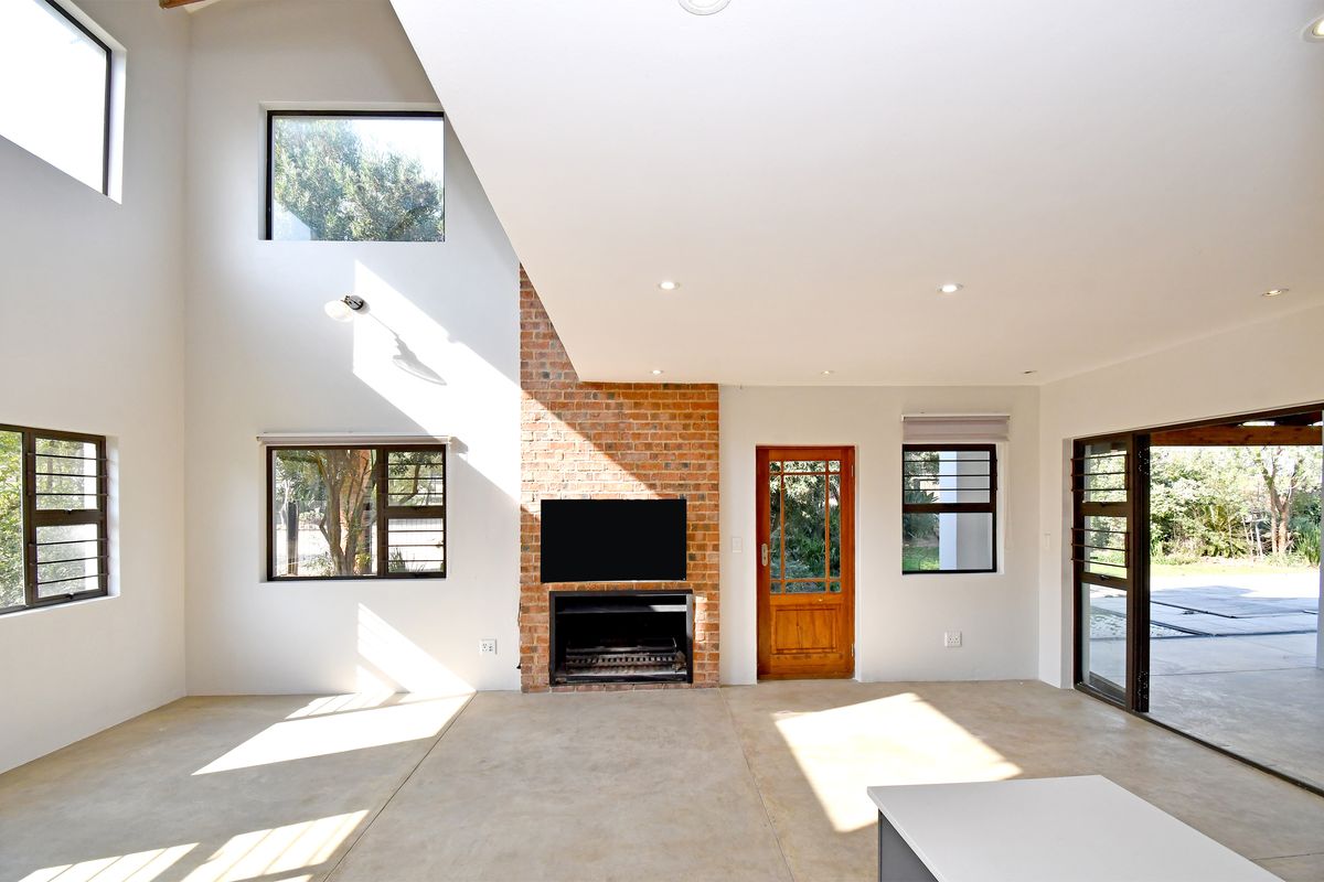 Spacious living area featuring high ceilings, exposed brick fireplace, polished concrete floors, and large windows providing abundant natural light and garden access.