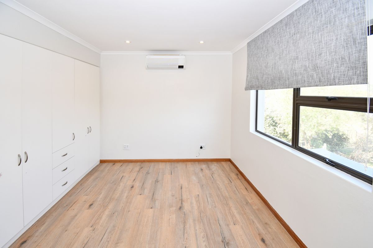 A bright, empty bedroom featuring modern laminate flooring, built-in cupboards, and a wall-mounted air conditioning unit.