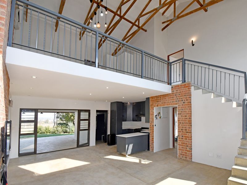 Spacious open-plan living area featuring double-volume ceilings with exposed timber trusses, a mezzanine level, concrete floors, and direct access to the outdoor patio.