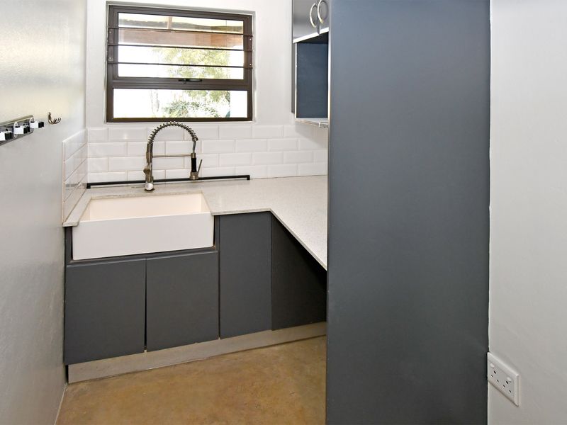 A clean and modern scullery featuring a farmhouse sink, gooseneck faucet, subway tile backsplash, and dark grey cabinetry with stone countertops.