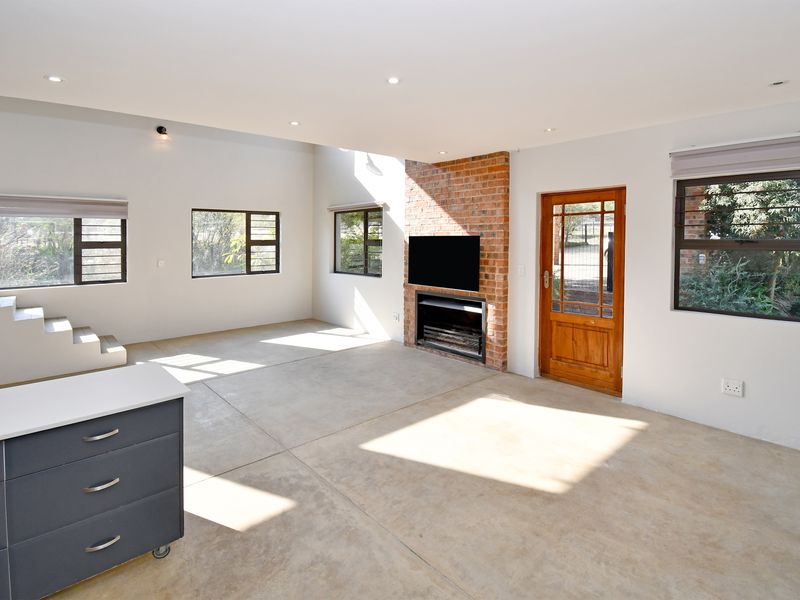 Spacious open-plan living area featuring polished concrete floors, an exposed brick fireplace, and abundant natural light through large windows.