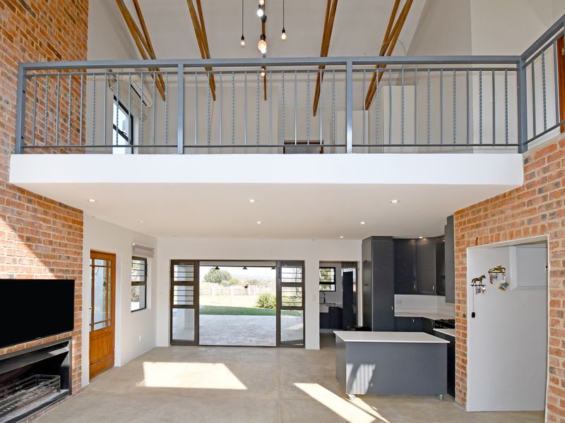 Spacious open-plan living area featuring exposed brick walls, timber ceiling beams, a mezzanine level, and a modern kitchen with a central island.