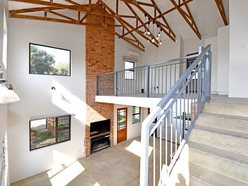 Spacious double-volume living area featuring exposed timber trusses, a prominent brick fireplace, concrete flooring, and a mezzanine level with metal railings.