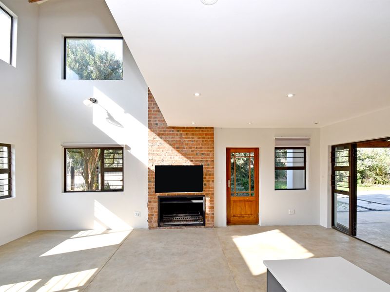 Spacious living area featuring high ceilings, exposed brick fireplace, polished concrete floors, and large windows providing abundant natural light and garden access.