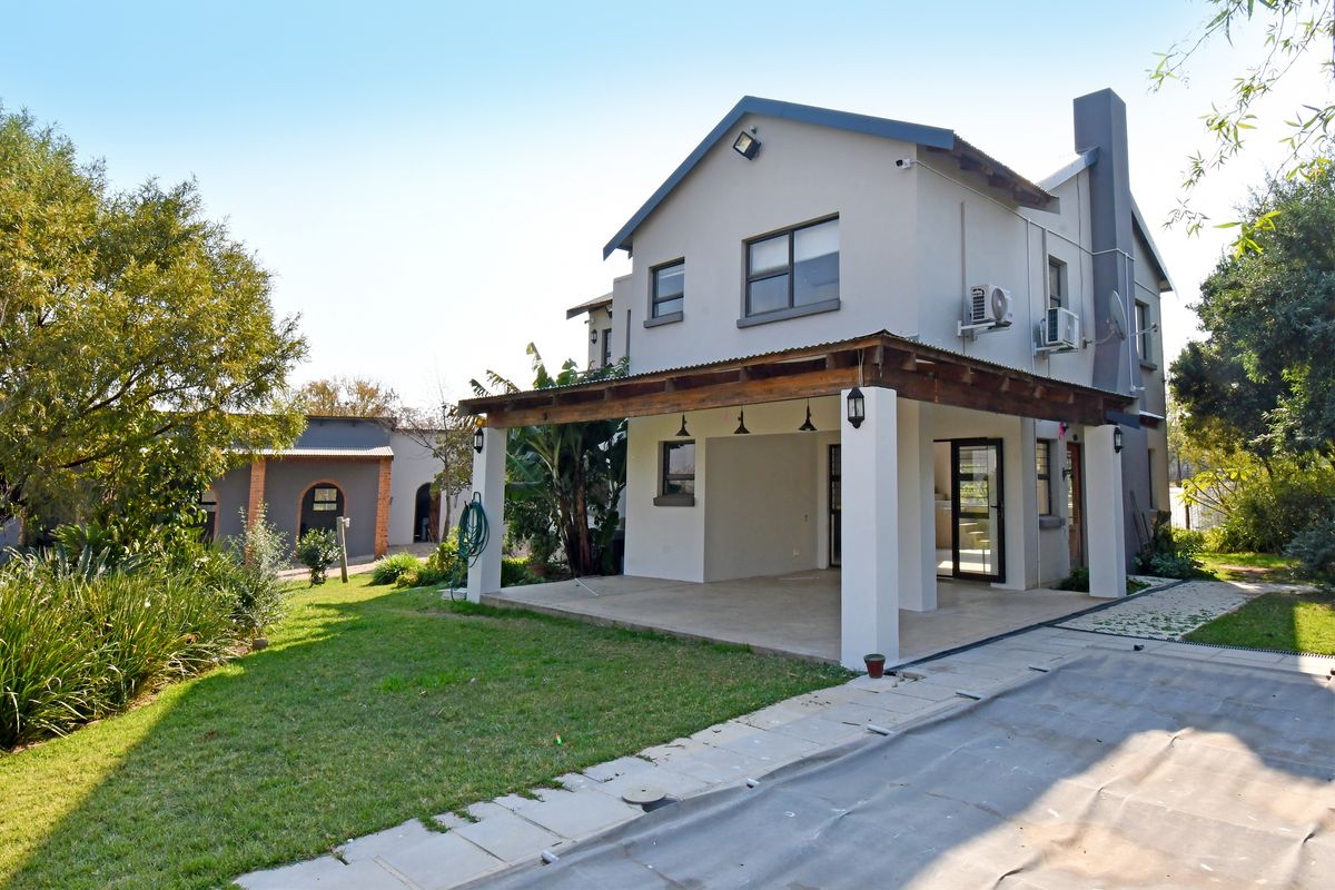 Rear view of the property featuring a covered patio with a timber pergola, landscaped garden, and external air conditioning units.