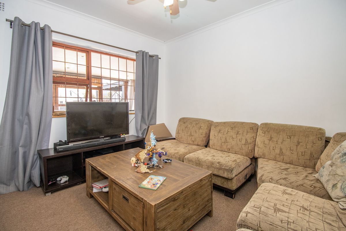A living room featuring carpet flooring, a ceiling fan, and a timber-framed window with curtains.