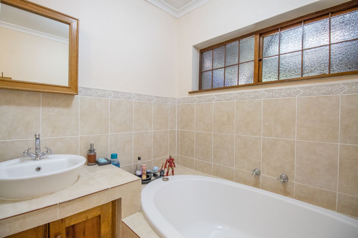 A functional bathroom featuring a built-in bathtub, vanity with ceramic basin, and tiled wall finishes with a timber-framed window.