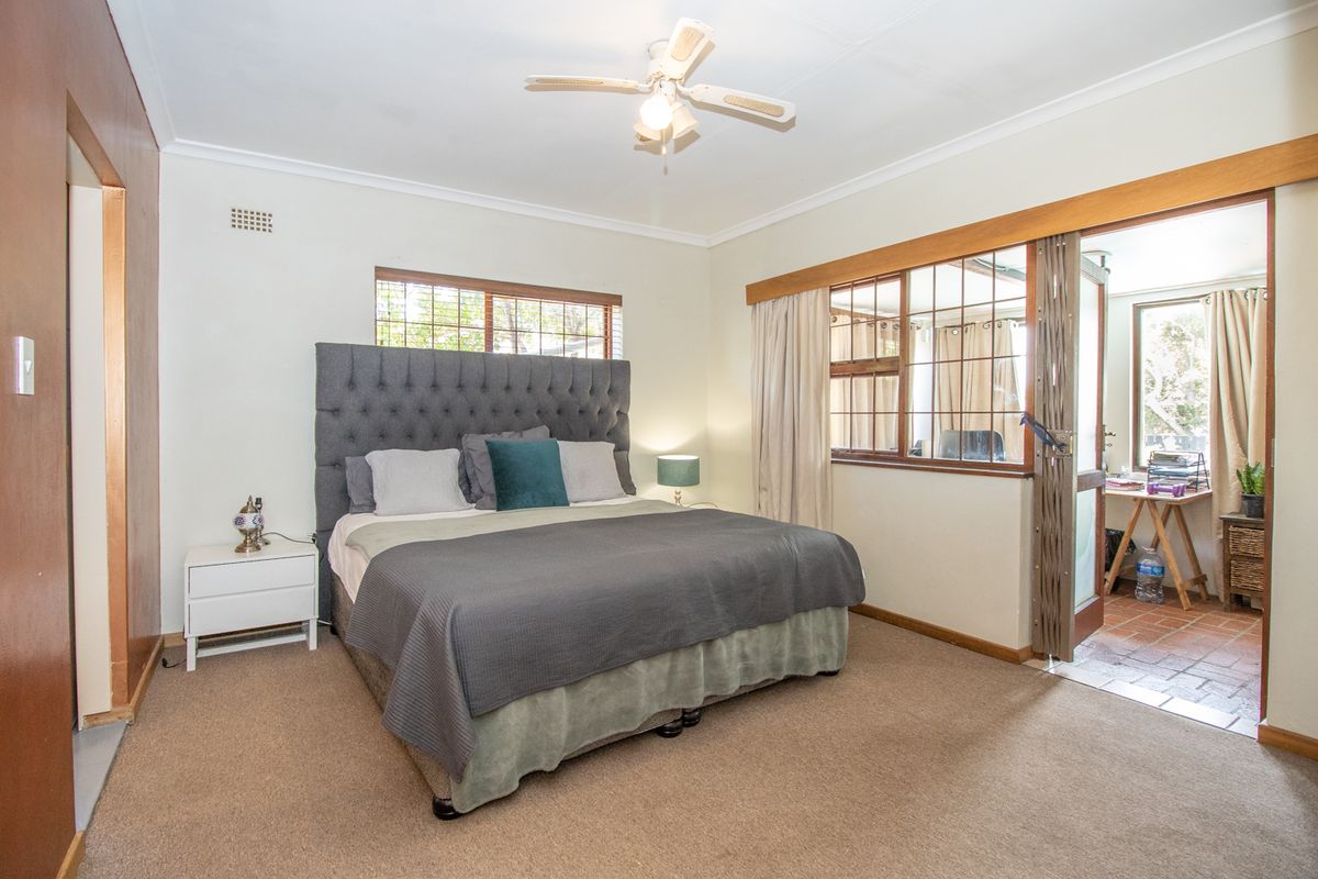 A spacious bedroom featuring carpeted flooring, a ceiling fan, and large windows with timber frames, providing access to an adjoining sunroom area.