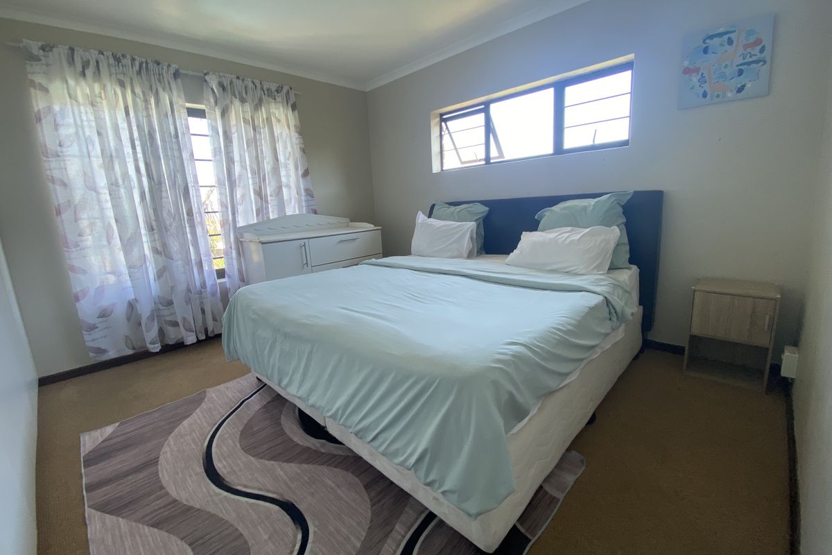 A functional bedroom featuring carpeted flooring, neutral wall tones, and natural light provided by top-hung windows.