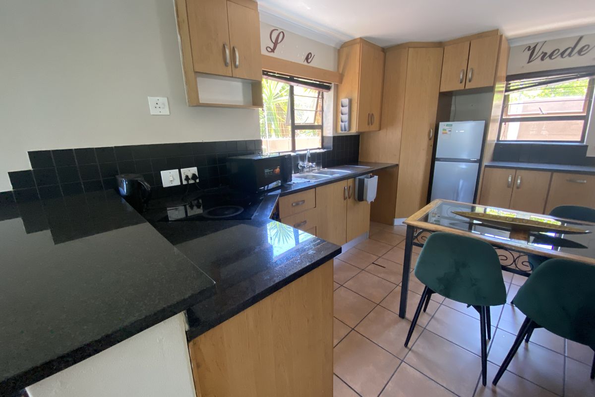 Functional kitchen featuring wooden cabinetry, black granite countertops, tiled backsplash, and tiled flooring with an integrated dining area.