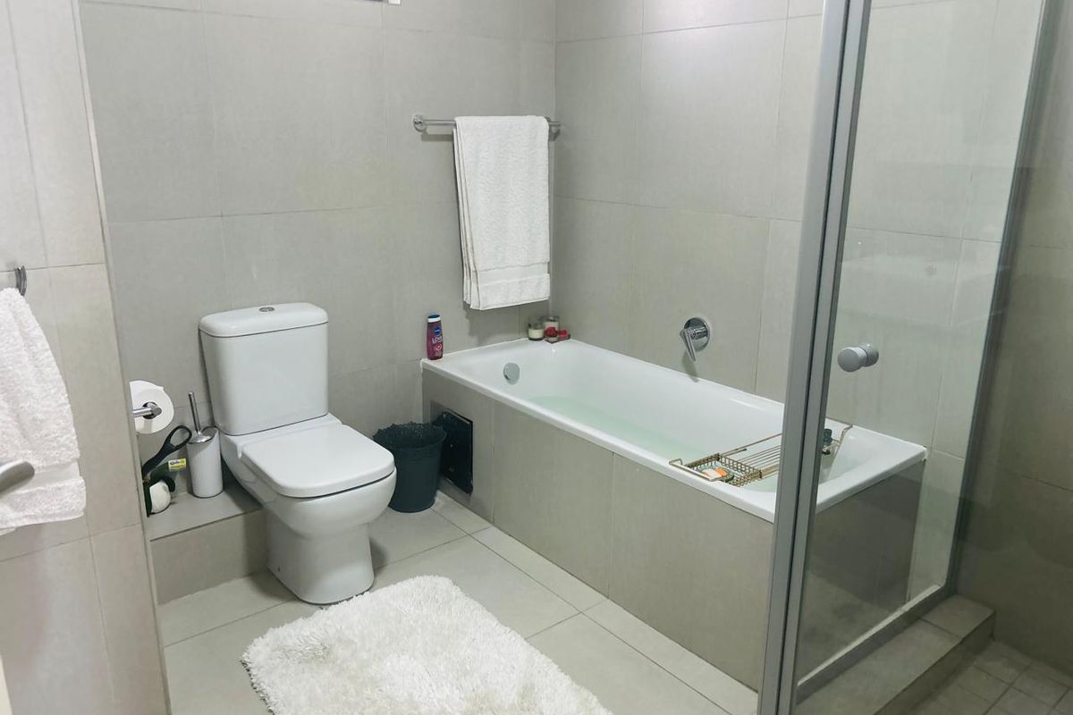 A modern bathroom featuring neutral wall and floor tiles, a built-in bathtub, a separate shower enclosure, and a standard toilet.