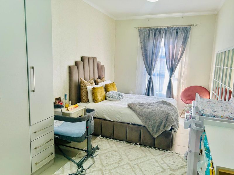 A well-lit bedroom featuring neutral wall finishes, tiled flooring, and a functional built-in wardrobe providing ample storage space.
