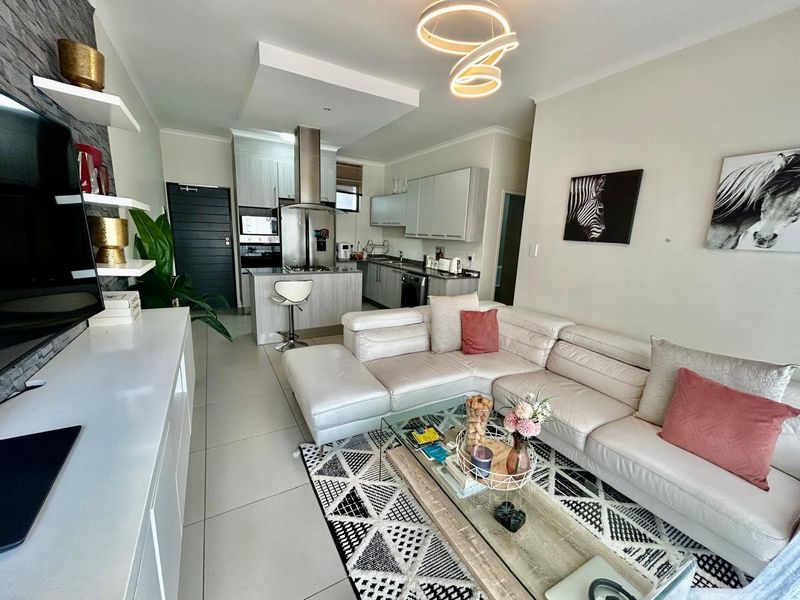 Modern open-plan living area featuring a sleek kitchen with built-in appliances, stone countertops, and tiled flooring, seamlessly flowing into the comfortable lounge space.