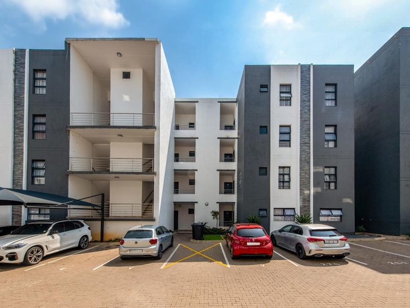 Modern multi-story apartment complex featuring a paved parking area, carports, and private balconies for each unit.
