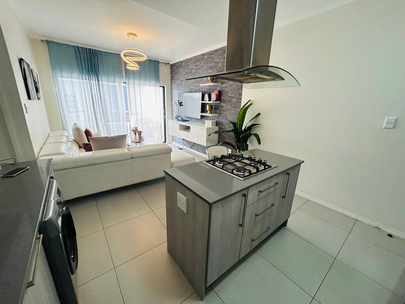 Modern open-plan living area featuring a kitchen island with gas hob, extractor fan, and contemporary finishes, seamlessly flowing into the lounge space.