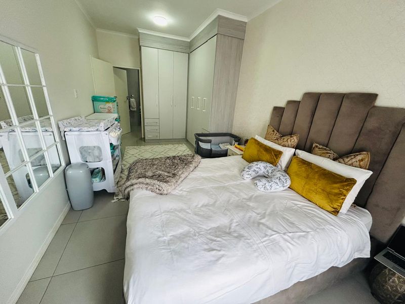 A well-maintained bedroom featuring neutral tiled flooring, built-in cabinetry, and a modern upholstered headboard, offering a functional and comfortable living space.