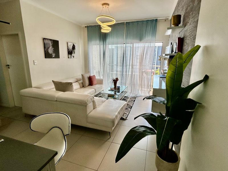 A bright and modern living room featuring tiled flooring, a textured feature wall, and a large sliding glass door leading to an outdoor area.
