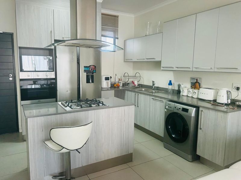 Modern kitchen featuring light wood-grain cabinetry, stone countertops, a gas hob with extractor fan, built-in oven, and integrated space for laundry appliances.