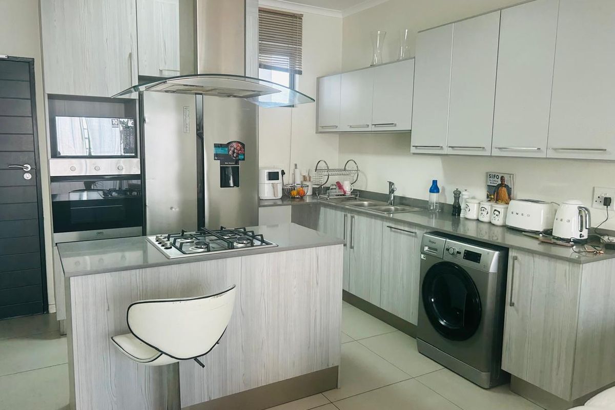 Modern kitchen featuring light wood-grain cabinetry, stone countertops, a gas hob with extractor fan, built-in oven, and integrated space for laundry appliances.