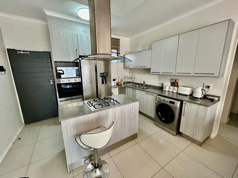 Modern kitchen featuring light wood-grain cabinetry, stone countertops, a central island with a gas hob, and integrated laundry facilities.