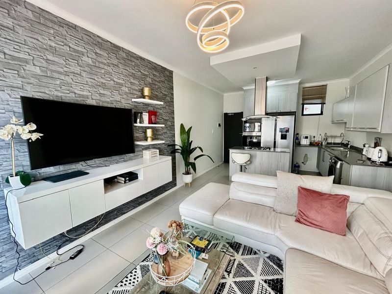 Modern open-plan living area featuring a stone veneer feature wall, sleek kitchen cabinetry, integrated appliances, and contemporary pendant lighting.