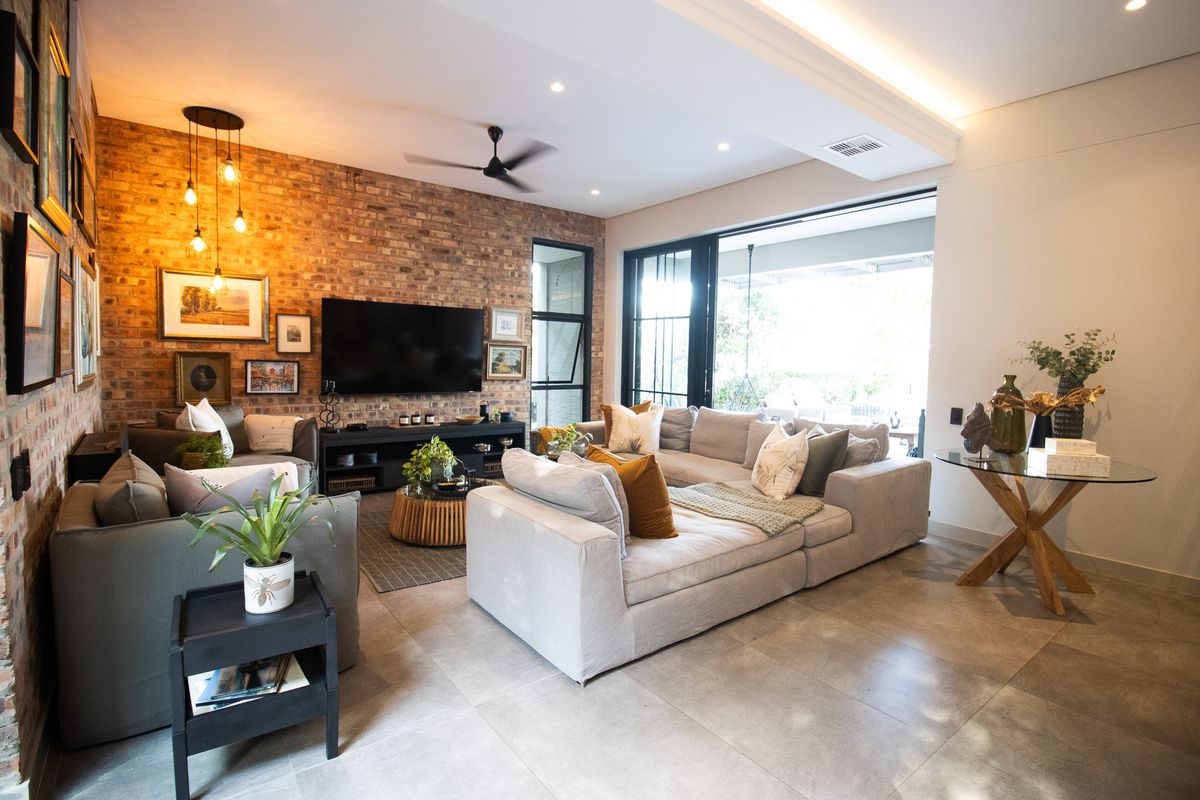 Spacious living room featuring an exposed brick feature wall, recessed lighting, large sliding doors opening to the patio, and modern tiled flooring.