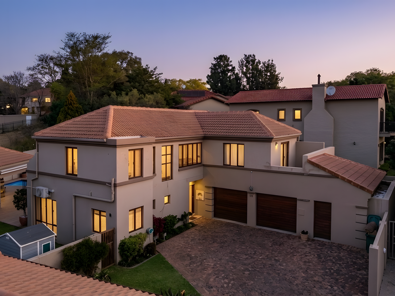 A well-maintained double-story residential property featuring a paved driveway, double garage, and terracotta roof tiles, captured during twilight.