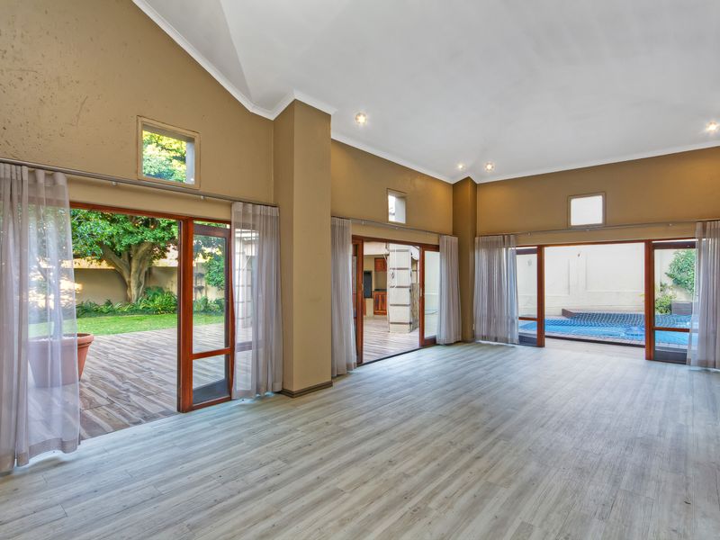 Spacious living area featuring vaulted ceilings, light laminate flooring, and multiple sliding glass doors providing seamless access to the outdoor deck and pool area.