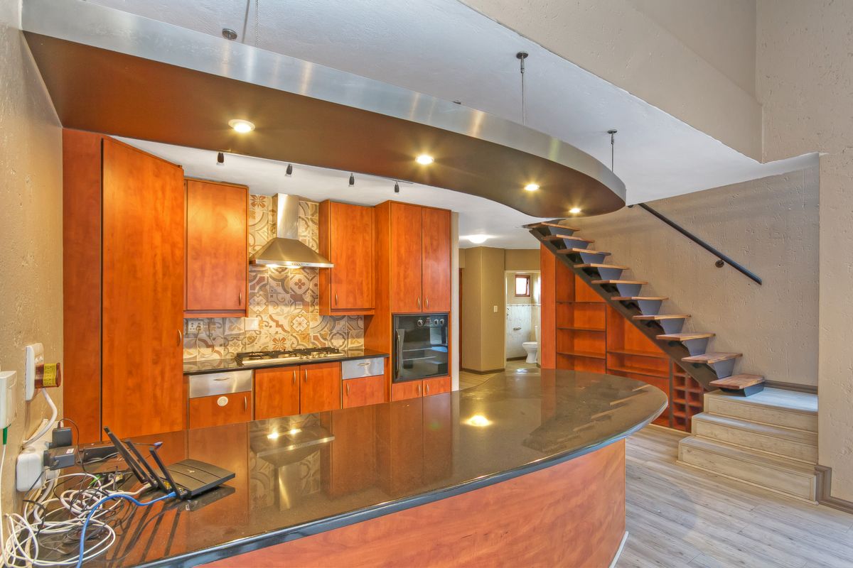 Open-plan kitchen featuring warm wood cabinetry, granite countertops, a gas hob, and a unique curved bulkhead with integrated lighting, adjacent to a staircase.