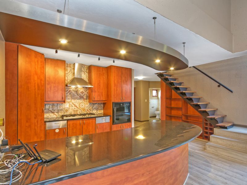 Open-plan kitchen featuring warm wood cabinetry, granite countertops, a gas hob, and a unique curved bulkhead with integrated lighting, adjacent to a staircase.