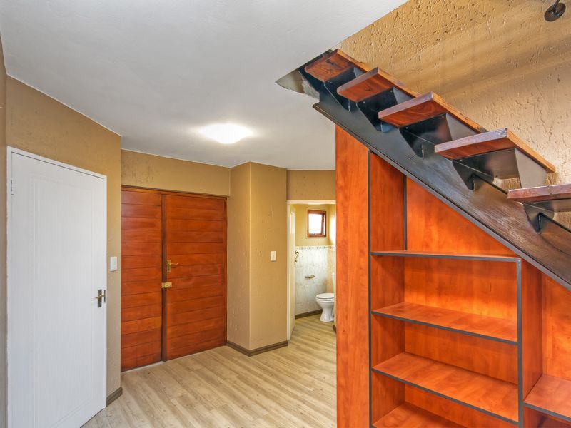 A spacious hallway featuring a modern staircase with built-in timber shelving underneath, leading towards a separate bathroom area.