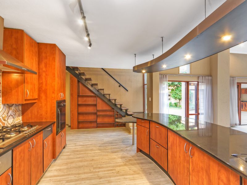 Open-plan kitchen featuring warm wood cabinetry, granite countertops, integrated appliances, and a feature staircase leading to the upper level.