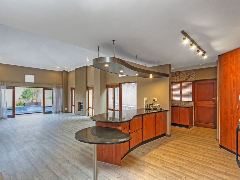 Spacious open-plan living and kitchen area featuring a unique curved island, built-in cabinetry, fireplace, and direct access to the outdoor pool area.